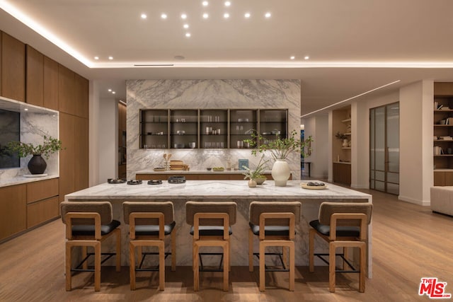 bar featuring light wood-type flooring, backsplash, and built in shelves