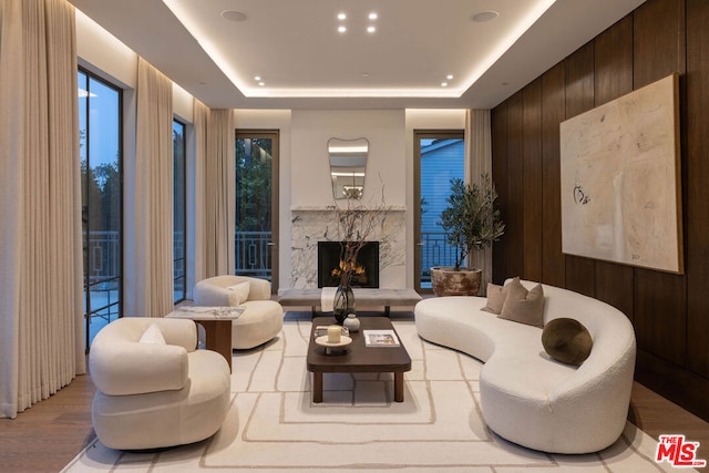 living room with light hardwood / wood-style floors, a premium fireplace, a raised ceiling, and wood walls