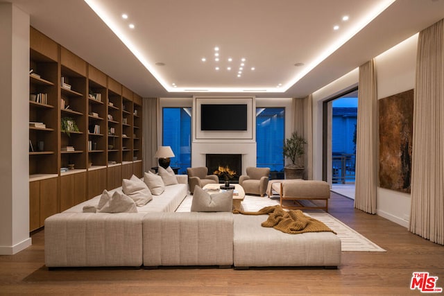 living room with wood-type flooring, a raised ceiling, and built in shelves