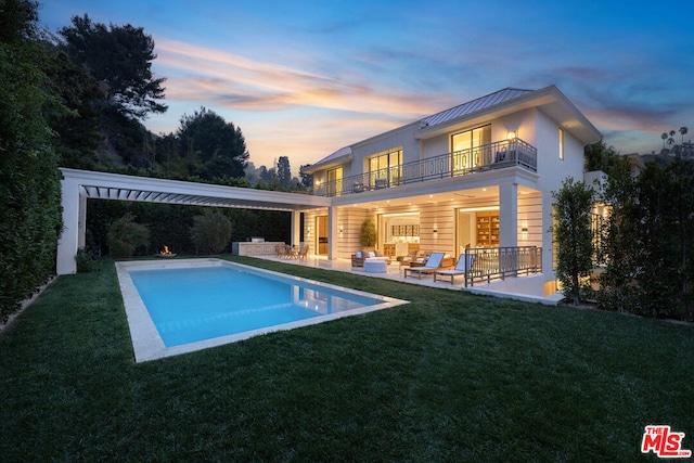 back house at dusk with an outdoor living space, a yard, a patio area, and a balcony