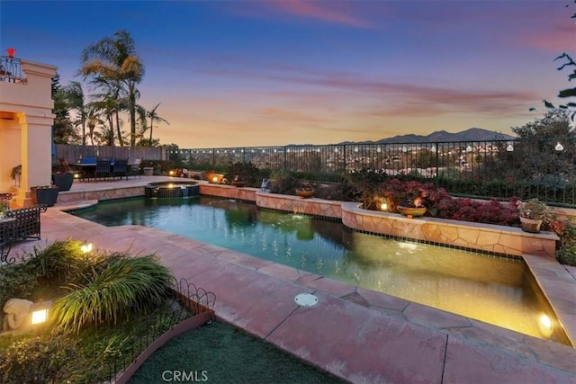 pool at dusk with an in ground hot tub and a patio area