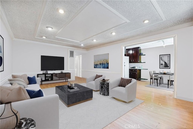 living room featuring a textured ceiling, light hardwood / wood-style flooring, crown molding, and a tray ceiling