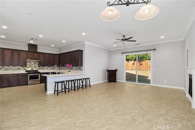 kitchen with a breakfast bar, stainless steel range oven, dark brown cabinets, decorative light fixtures, and tasteful backsplash