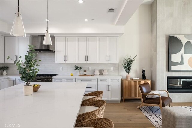 kitchen with pendant lighting, tasteful backsplash, white cabinets, a tiled fireplace, and wall chimney exhaust hood