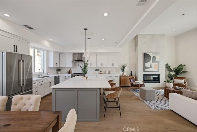 kitchen featuring wall chimney range hood, high quality fridge, white cabinets, and a kitchen island