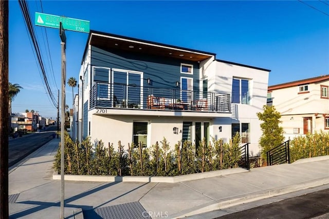 view of front of home featuring fence, a balcony, and stucco siding