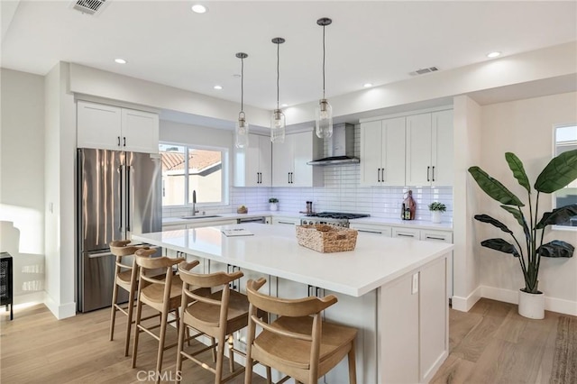 kitchen featuring wall chimney range hood, white cabinetry, appliances with stainless steel finishes, and a center island