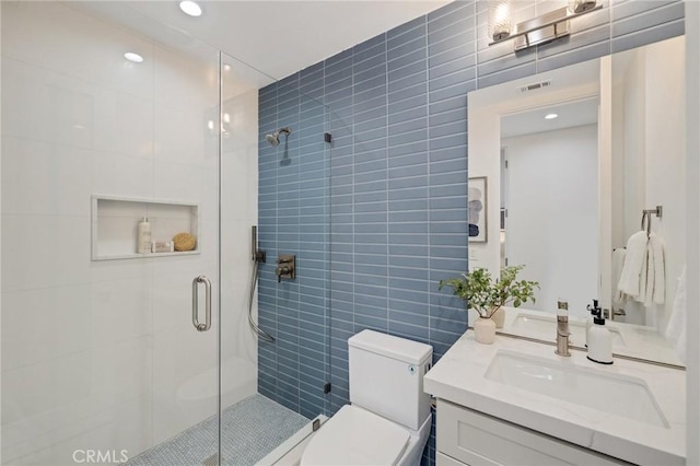 bathroom featuring vanity, toilet, tile walls, and a shower with door