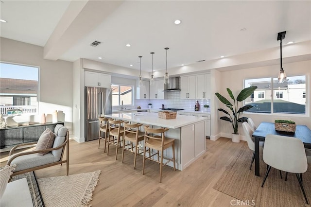 kitchen featuring decorative light fixtures, a kitchen island, high end fridge, white cabinets, and wall chimney exhaust hood