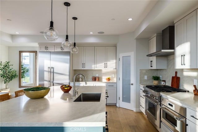 kitchen with wall chimney exhaust hood, sink, white cabinetry, premium appliances, and pendant lighting