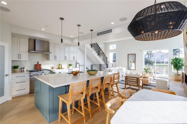 kitchen with sink, white cabinets, a kitchen island with sink, high end stainless steel range, and wall chimney range hood