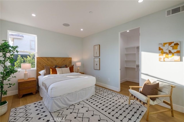 bedroom featuring a walk in closet, a closet, and light hardwood / wood-style flooring