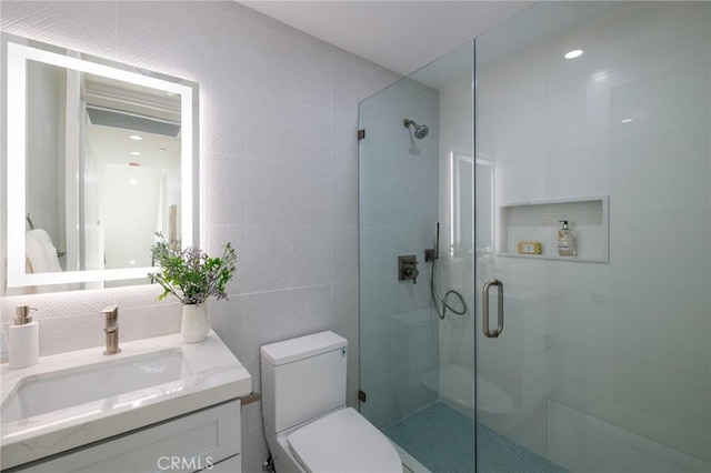 bathroom featuring vanity, a shower with door, toilet, and tile walls