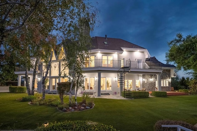 rear view of house with a balcony, a patio, and a lawn