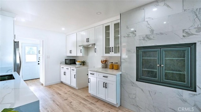 kitchen with light stone counters, stainless steel fridge, light hardwood / wood-style floors, and white cabinets