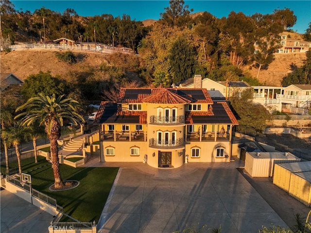 view of front of home with a balcony, a chimney, fence, and stucco siding