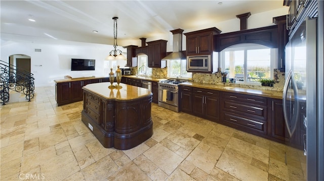 kitchen featuring a center island, pendant lighting, stainless steel appliances, stone tile flooring, and wall chimney exhaust hood