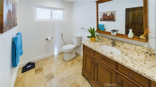 bathroom with stone finish floor, baseboards, vanity, and toilet