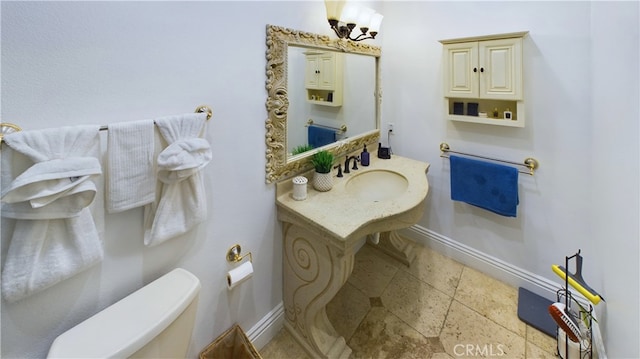 bathroom with stone tile flooring, a sink, toilet, and baseboards