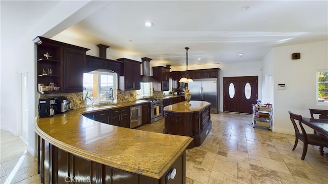 kitchen featuring stainless steel appliances, wall chimney exhaust hood, a kitchen island, and decorative light fixtures