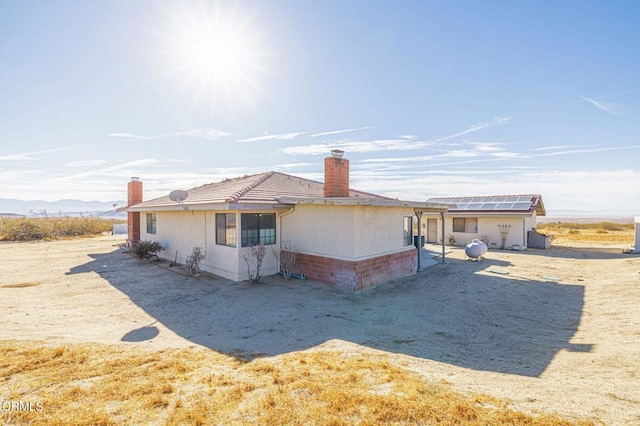 back of property with a mountain view and solar panels