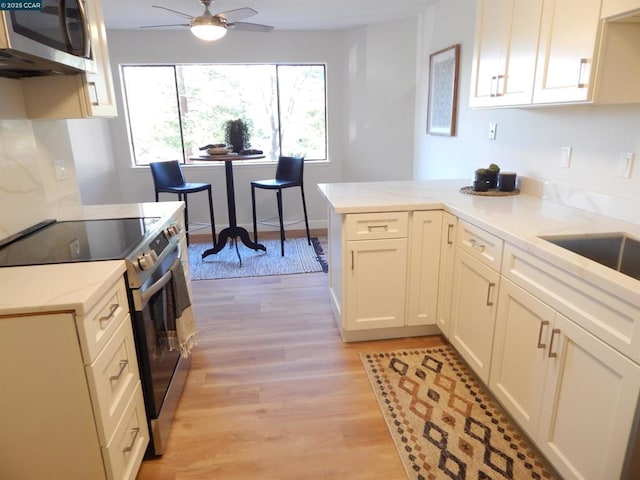 kitchen featuring light hardwood / wood-style floors, stainless steel appliances, kitchen peninsula, ceiling fan, and sink