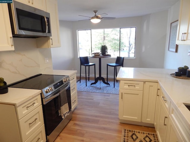 kitchen with light stone counters, appliances with stainless steel finishes, ceiling fan, and light hardwood / wood-style floors