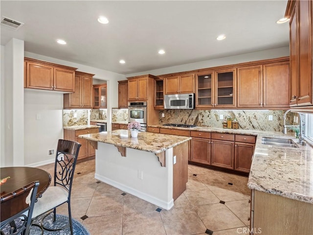 kitchen featuring a kitchen island, light stone countertops, appliances with stainless steel finishes, and sink