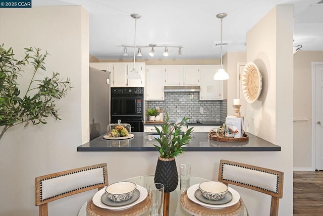 kitchen with decorative light fixtures, backsplash, stainless steel fridge, white cabinets, and black double oven