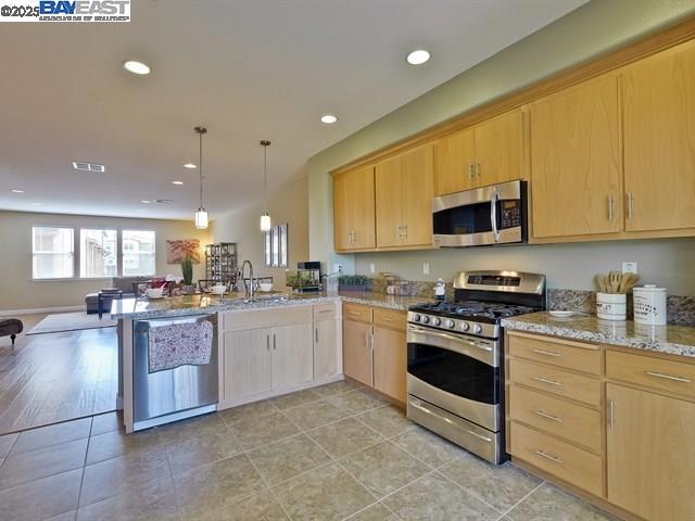 kitchen with stainless steel appliances, light brown cabinetry, kitchen peninsula, and decorative light fixtures