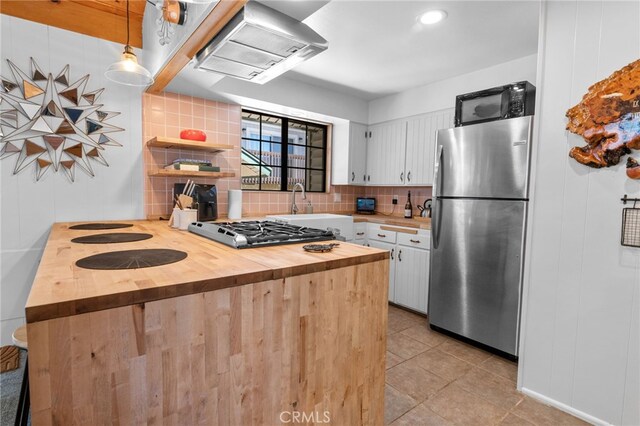 kitchen with stainless steel appliances, white cabinets, decorative light fixtures, wall chimney exhaust hood, and wooden counters