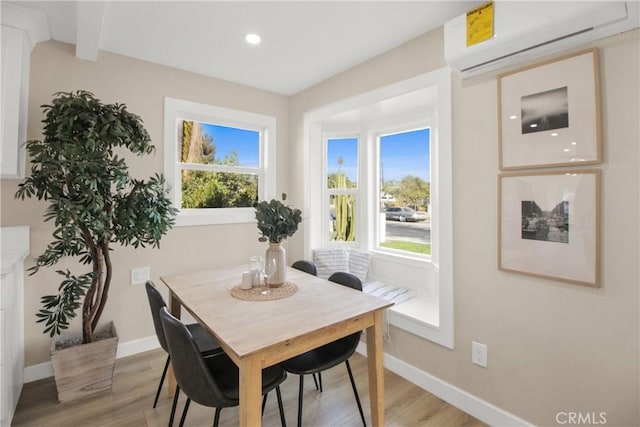 dining space featuring a wall unit AC, light wood-type flooring, and a wealth of natural light