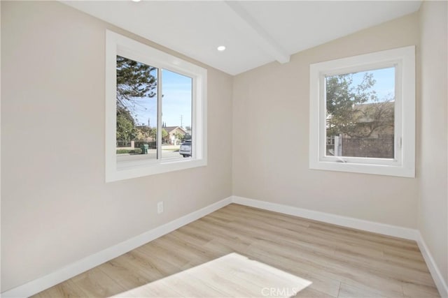 empty room with light hardwood / wood-style flooring and beamed ceiling