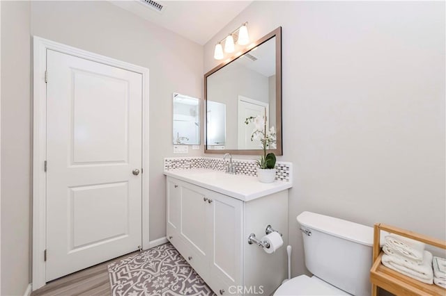 bathroom with toilet, vanity, backsplash, and hardwood / wood-style flooring