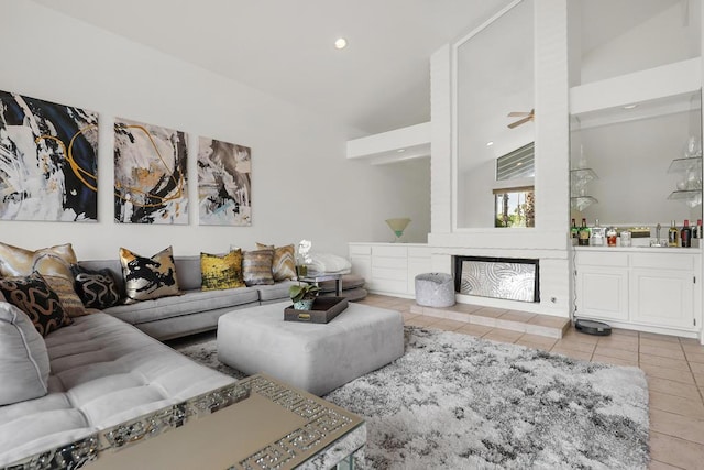 tiled living room with a tiled fireplace, ceiling fan, and vaulted ceiling