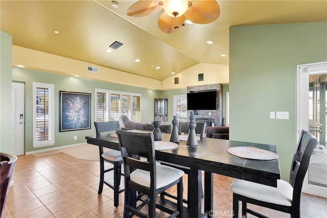 tiled dining space with ceiling fan, vaulted ceiling, and a stone fireplace