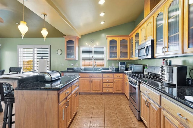 kitchen featuring vaulted ceiling, pendant lighting, a kitchen bar, appliances with stainless steel finishes, and dark stone countertops