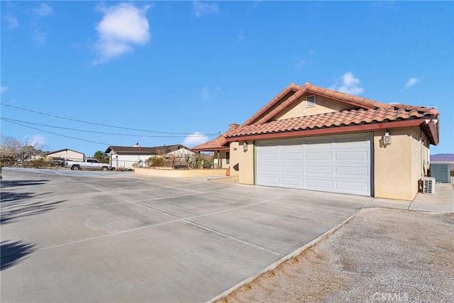 32758 Spinel Rd, Lucerne Valley, CA 92356 - view of side of home with concrete driveway, stucco siding, an attached garage, a tiled roof, and central AC unit