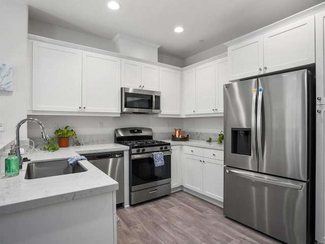 kitchen with stainless steel appliances, sink, white cabinets, light wood-type flooring, and light stone countertops