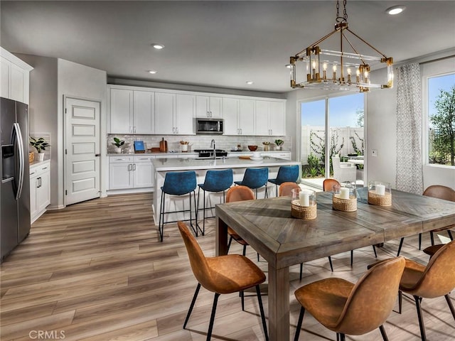 kitchen with stainless steel appliances, white cabinets, backsplash, hanging light fixtures, and a center island with sink