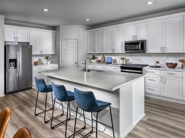 kitchen featuring a kitchen island with sink, stainless steel appliances, a breakfast bar, sink, and white cabinetry