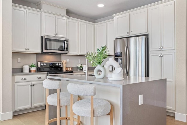 kitchen featuring white cabinetry, an island with sink, a breakfast bar area, stainless steel appliances, and light wood-type flooring