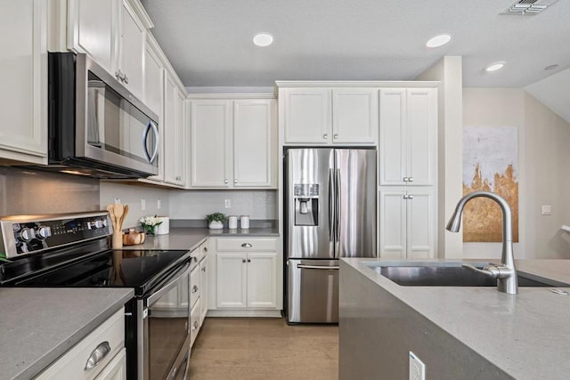 kitchen featuring appliances with stainless steel finishes, light hardwood / wood-style flooring, white cabinets, and sink