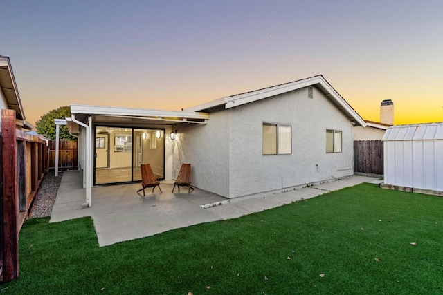 back house at dusk with a yard, a storage unit, and a patio