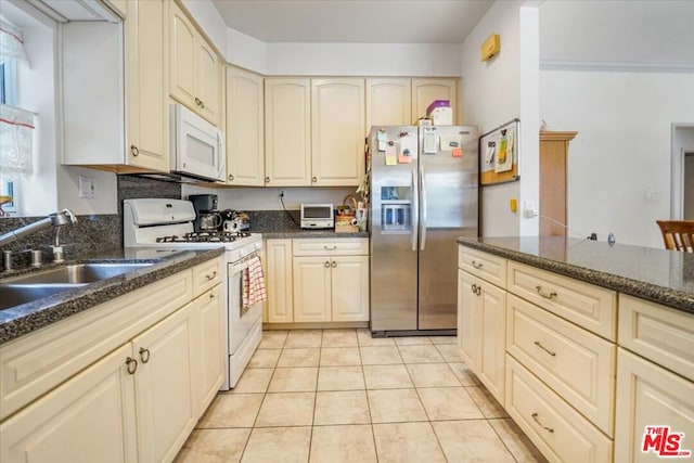 kitchen with white appliances, dark stone countertops, light tile patterned floors, and sink