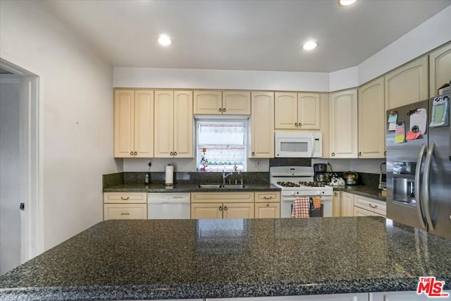 kitchen featuring white appliances, dark stone countertops, and sink