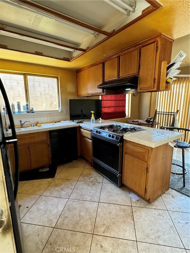 kitchen with kitchen peninsula, tile countertops, light tile patterned floors, black appliances, and sink