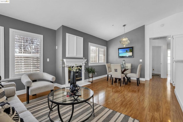 living room with vaulted ceiling, an inviting chandelier, and light hardwood / wood-style floors