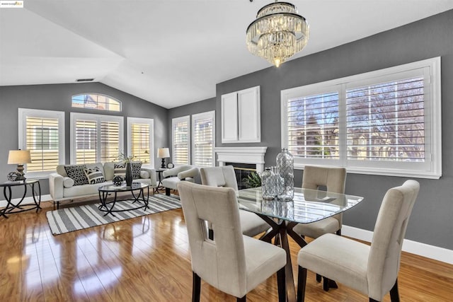 dining space with light wood-type flooring, an inviting chandelier, lofted ceiling, and a large fireplace