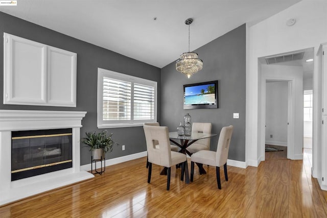 dining room featuring an inviting chandelier, light hardwood / wood-style flooring, and lofted ceiling